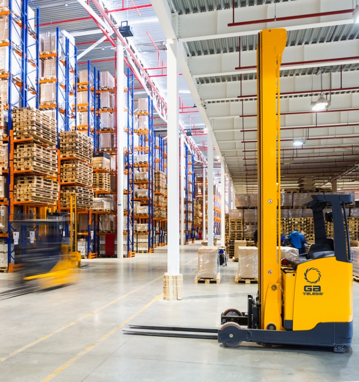 Forklift operating in a large warehouse with tall storage racks.